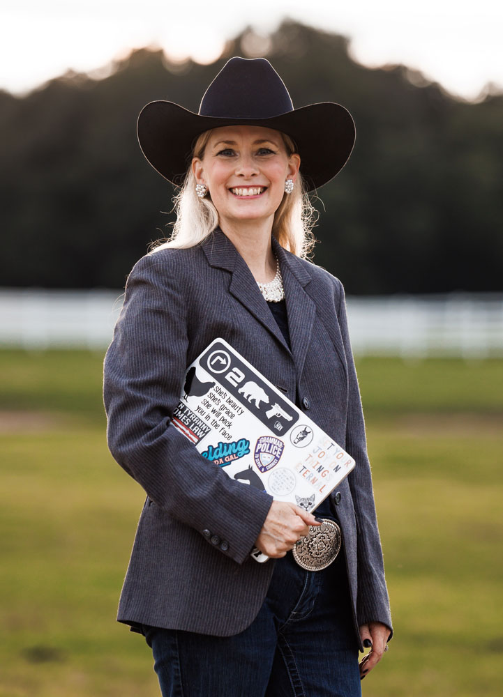 Jamie in horse pasture with dark blazer holding laptop