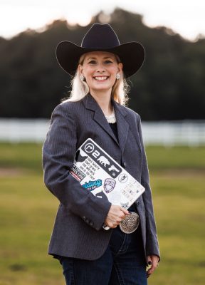 Computer-with-suit-jacket-and-smile Jamie in horse pasture with dark blazer holding laptop